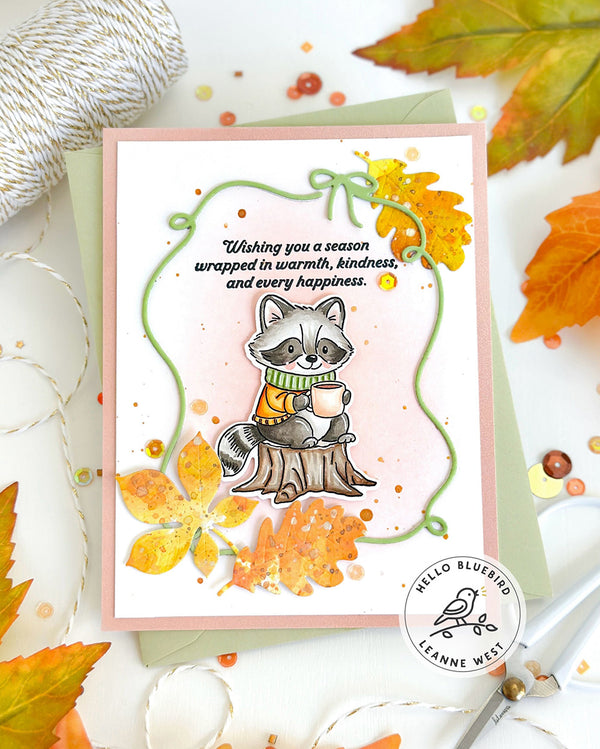 Autumn-themed card with a raccoon wearing a sweater and scarf, surrounded by leaves and yarn.